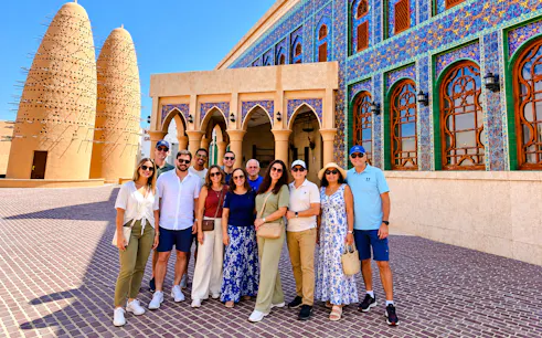 Group of tourists at Katara Cultural Village, Doha, with traditional architecture and pigeon towers.