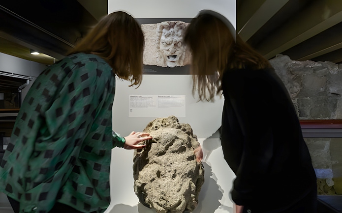 Visitors examining ancient stone artifact in Notre-Dame Archaeological Crypt, Paris.