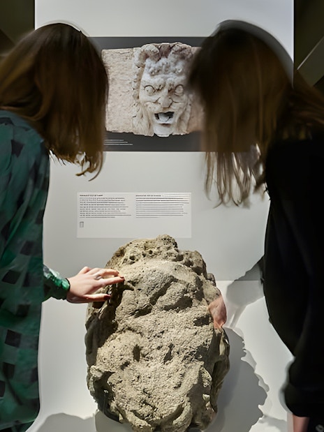 Visitors examining ancient stone artifact in Notre-Dame Archaeological Crypt, Paris.