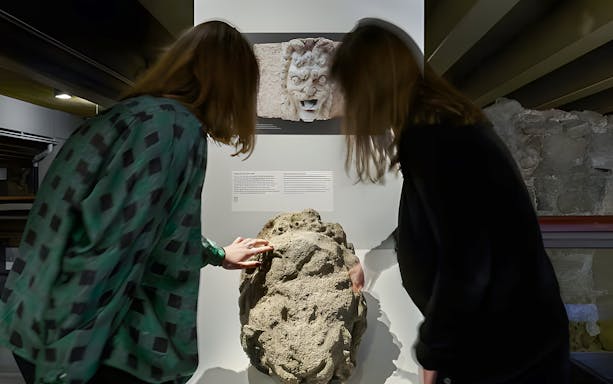 Visitors examining ancient stone artifact in Notre-Dame Archaeological Crypt, Paris.