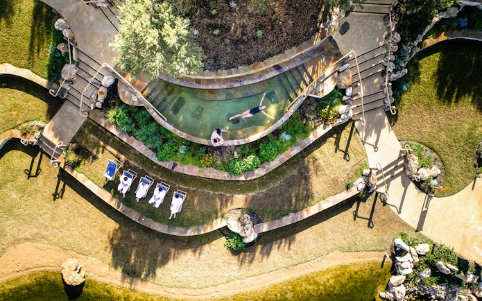 Aerial view of Peninsula Hot Springs pool with people relaxing and sunbathing nearby.