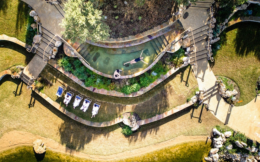 Aerial view of Peninsula Hot Springs pool with people relaxing and sunbathing nearby.