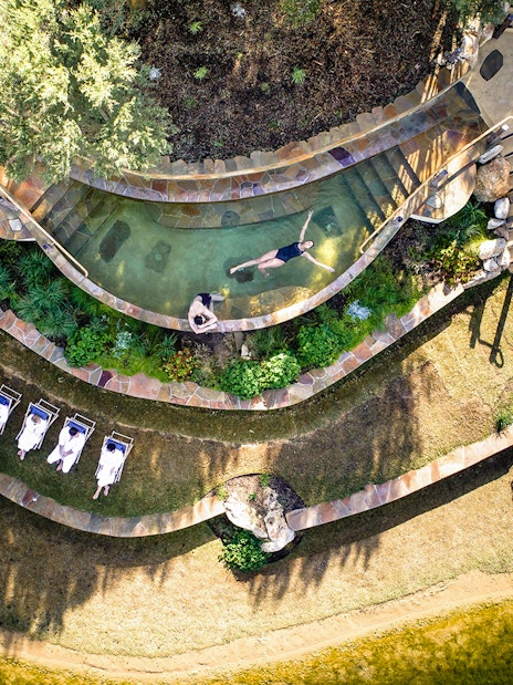 Aerial view of Peninsula Hot Springs pool with people relaxing and sunbathing nearby.