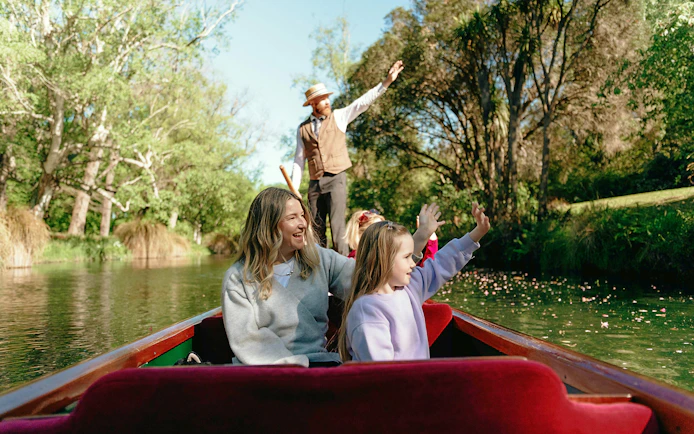 Punting on the Avon River in Christchurch with a guide and passengers enjoying the scenic view.