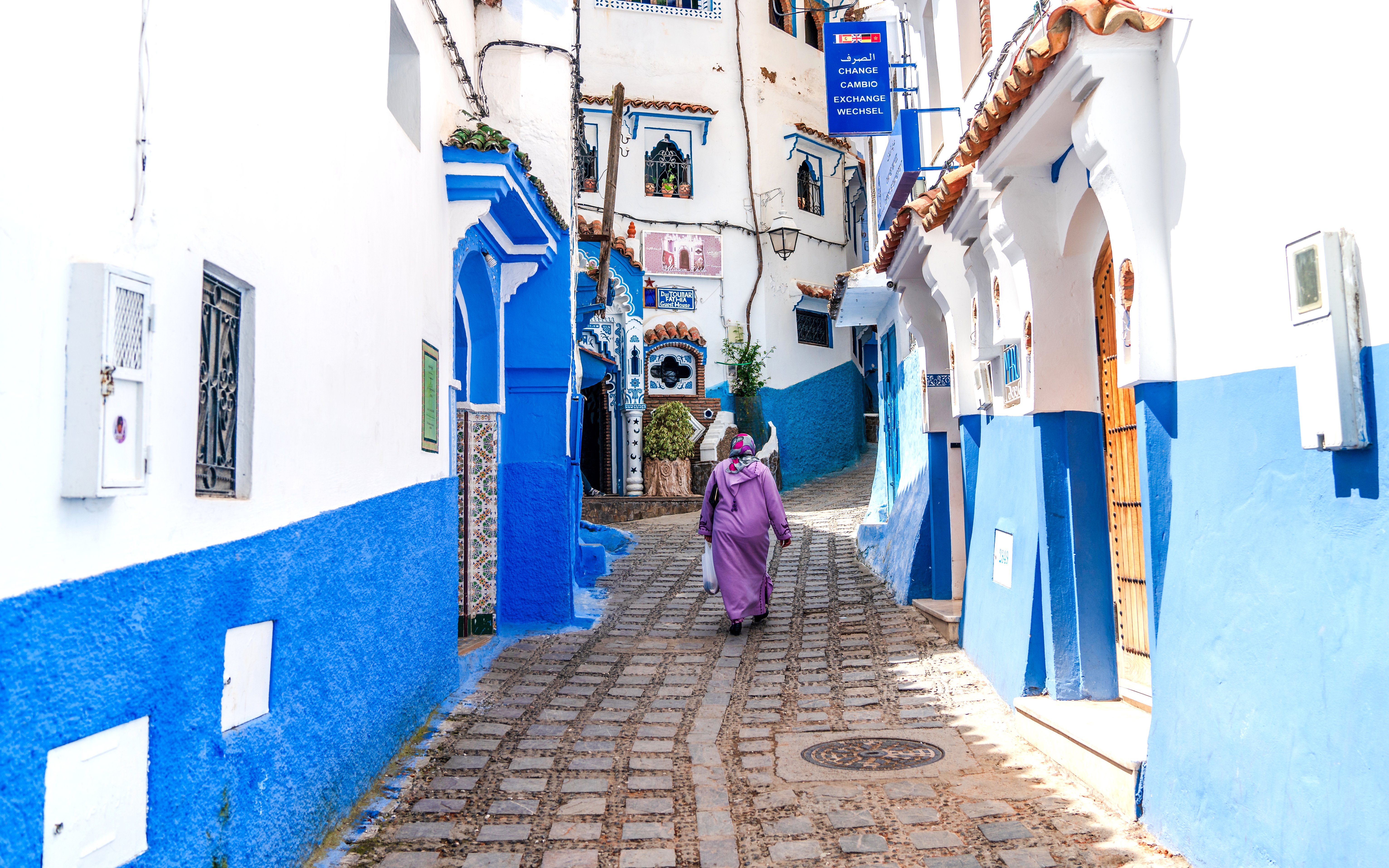 Woman walking through blue-painted alley in Chefchaouen, Morocco.