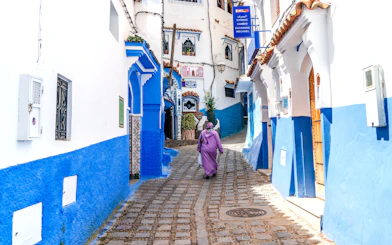 Woman walking through blue-painted alley in Chefchaouen, Morocco.