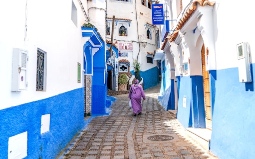 Woman walking through blue-painted alley in Chefchaouen, Morocco.