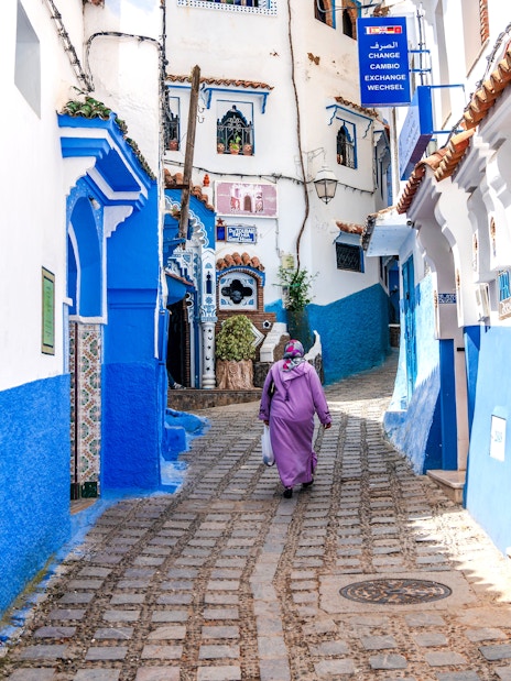 Woman walking through blue-painted alley in Chefchaouen, Morocco.