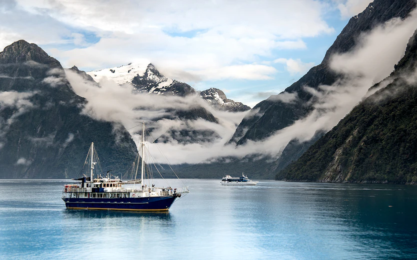 Cruise boat on Milford Sound with misty mountains, Te Anau to Milford tour.
