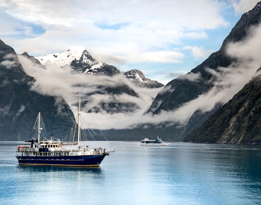 Cruise boat on Milford Sound with misty mountains, Te Anau to Milford tour.