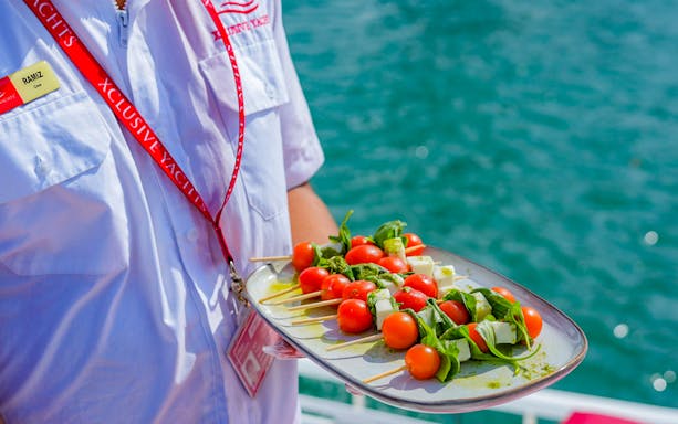 Crew member holding a platter of skewered appetizers on a Dubai Marina sailing tour.
