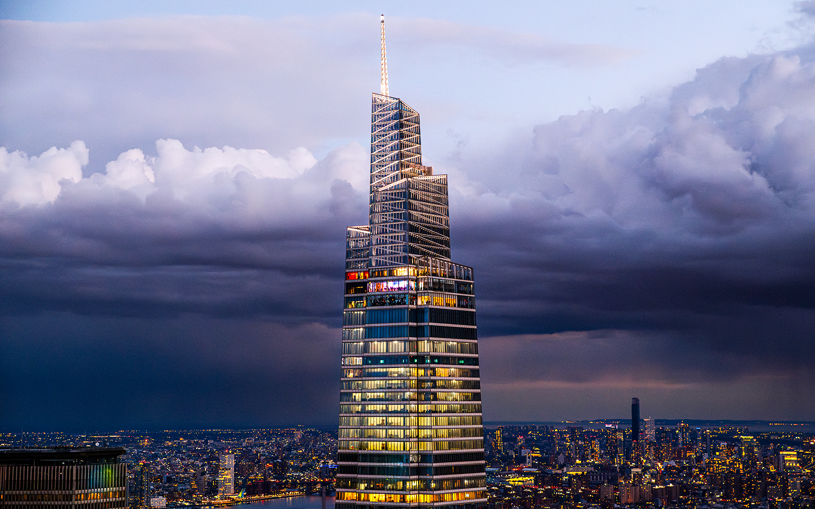 One Vanderbilt skyscraper lit up at dusk with New York City skyline in the background.