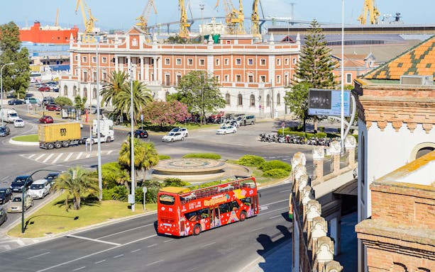 Hop-On Hop-Off bus passing by a historic building in Cadiz, Spain.