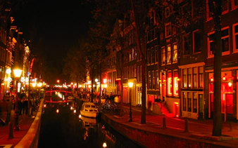 Canal view in Amsterdam's Red Light District at night with illuminated buildings.