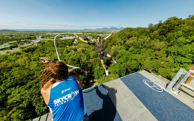 Person bungee jumping from a platform in Cairns, Australia, with a scenic forest and ocean view.