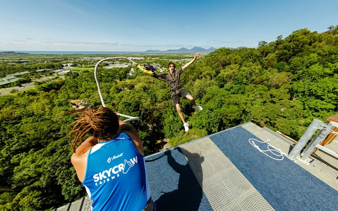Person bungee jumping from a platform in Cairns, Australia, with a scenic forest and ocean view.