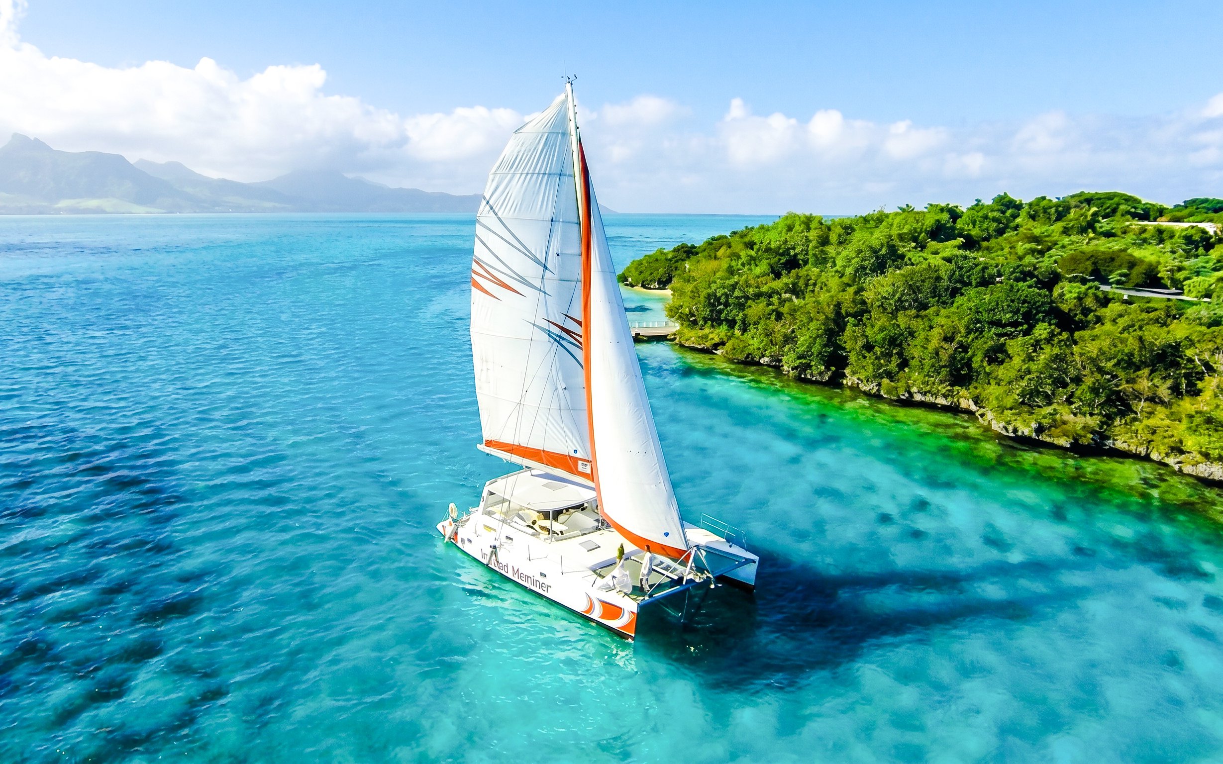 Catamaran sailing near Ile aux Cerf with lush greenery and clear blue waters.