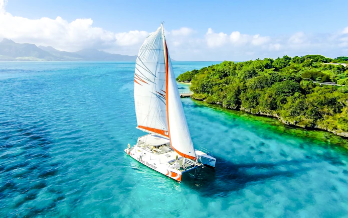 Catamaran sailing near Ile aux Cerf with lush greenery and clear blue waters.