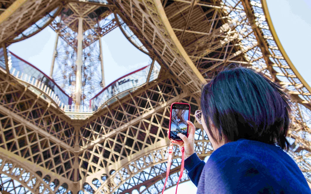 Person photographing Eiffel Tower structure during Paris Illumination Tour.