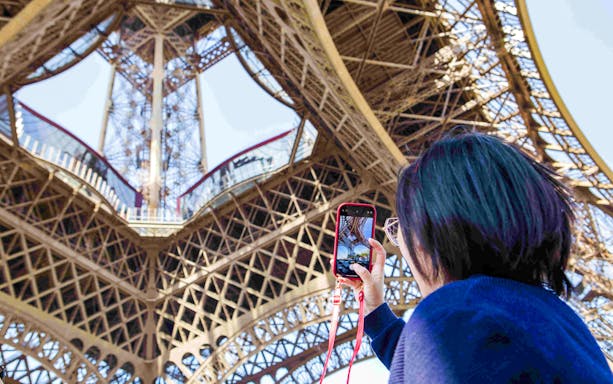 Person photographing Eiffel Tower structure during Paris Illumination Tour.