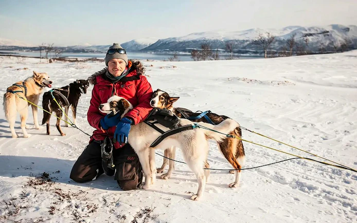 Guests interacting with huskies during self-drive sledding tour in snowy Tromso landscape.