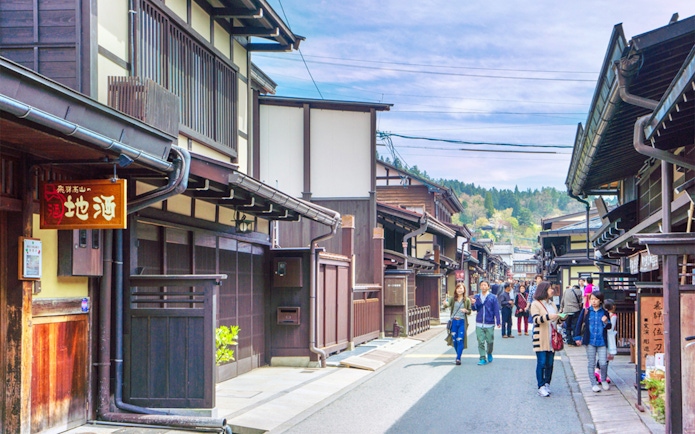 Street view of traditional wooden buildings in Takayama, Japan, with tourists exploring.