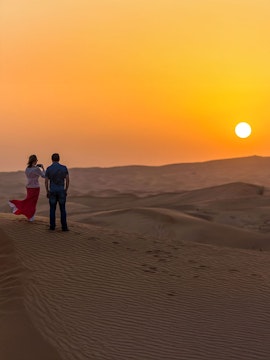 Couple standing on sand dune at sunset during desert safari.