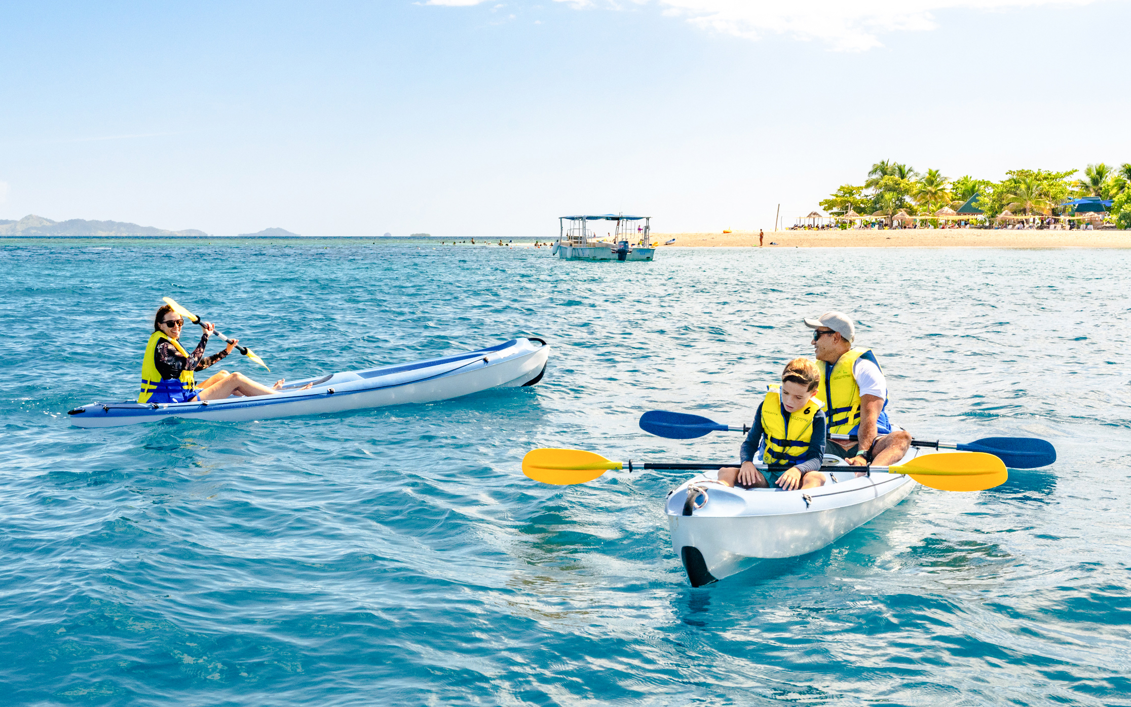 Family kayaking near South Sea Island, Fiji with clear blue water and distant beach.