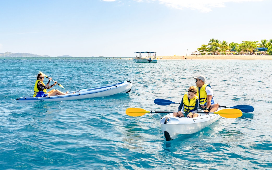 Family kayaking near South Sea Island, Fiji with clear blue water and distant beach.