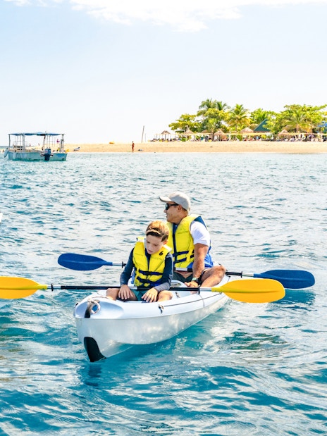 Family kayaking near South Sea Island, Fiji with clear blue water and distant beach.