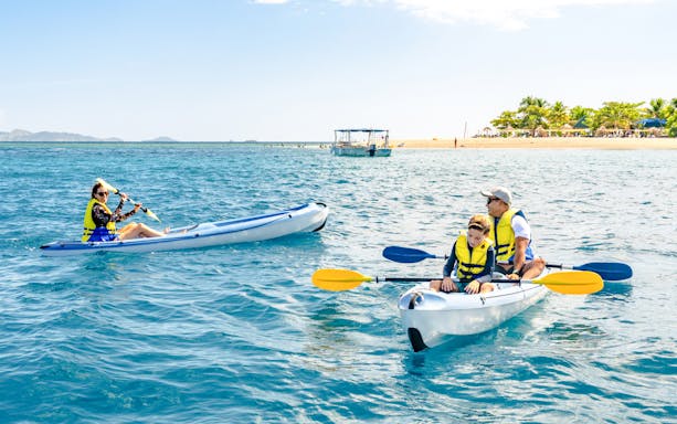 Family kayaking near South Sea Island, Fiji with clear blue water and distant beach.