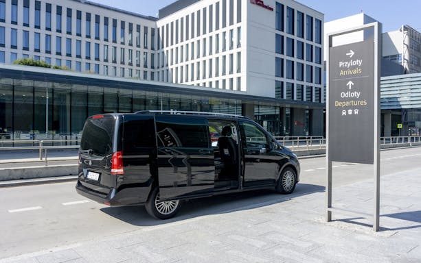 Black van parked at Krakow Airport terminal for private transfer service.