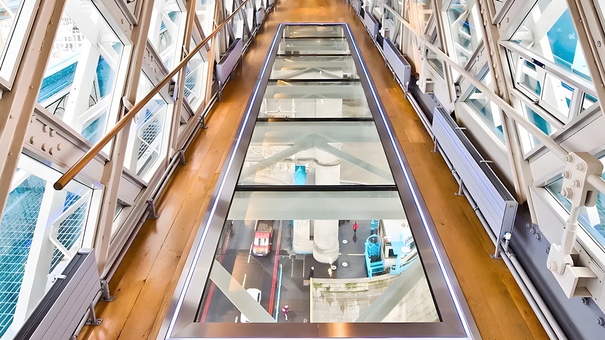 Glass walkway inside Tower Bridge, London, with view of the road and river below.