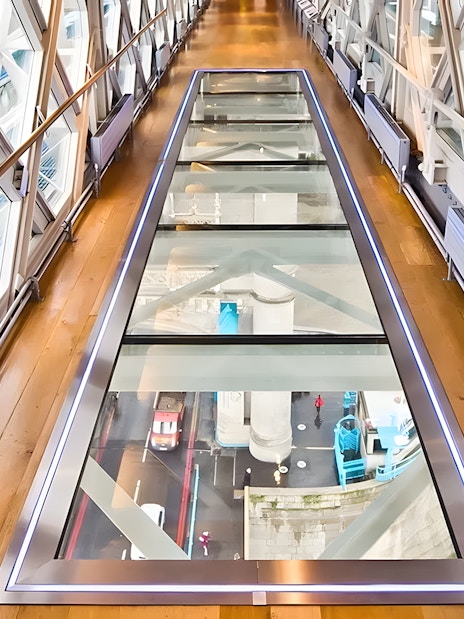 Glass walkway inside Tower Bridge, London, with view of the road and river below.