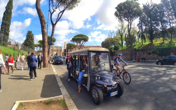 Golf cart tour near the Colosseum in Rome with tourists and cyclists nearby.