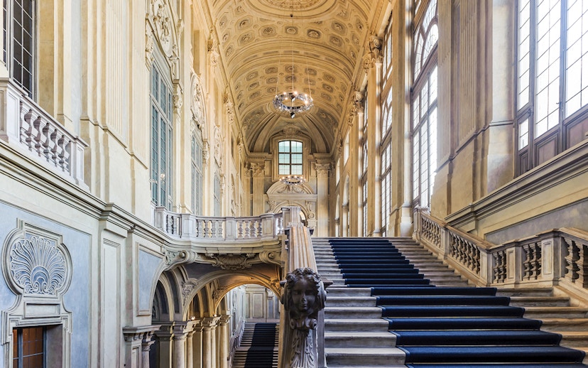 Grand staircase inside Royal Palace Museum with ornate ceiling and large windows.