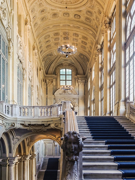 Grand staircase inside Royal Palace Museum with ornate ceiling and large windows.