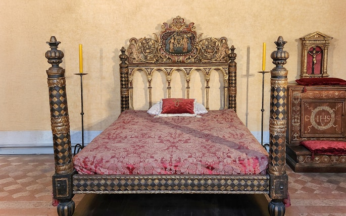 Ornate bed in Castel Sant'Angelo bedroom, Rome, with intricate carvings and red bedding.