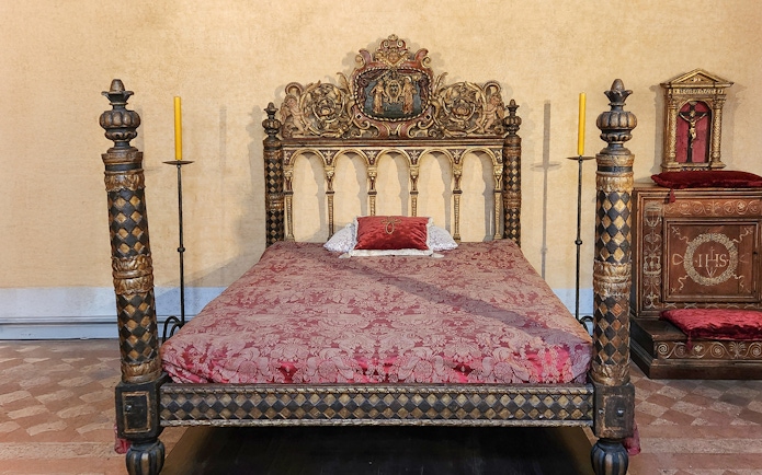 Ornate bed in Castel Sant'Angelo bedroom, Rome, with intricate carvings and red bedding.