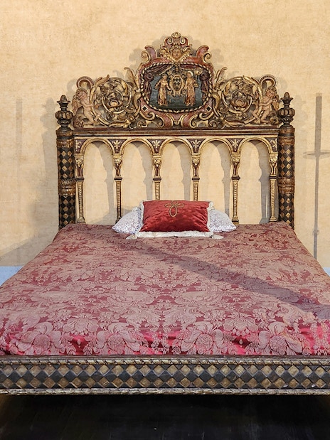 Ornate bed in Castel Sant'Angelo bedroom, Rome, with intricate carvings and red bedding.