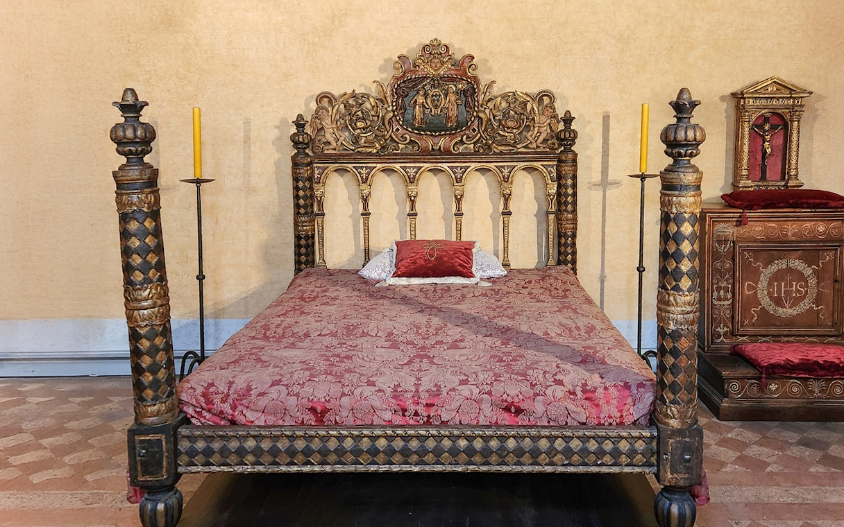 Ornate bed in Castel Sant'Angelo bedroom, Rome, with intricate carvings and red bedding.