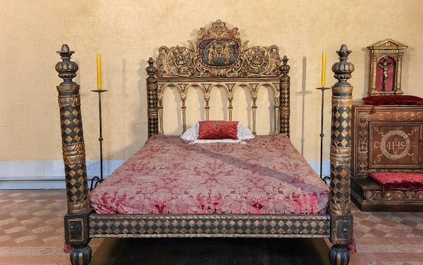 Ornate bed in Castel Sant'Angelo bedroom, Rome, with intricate carvings and red bedding.