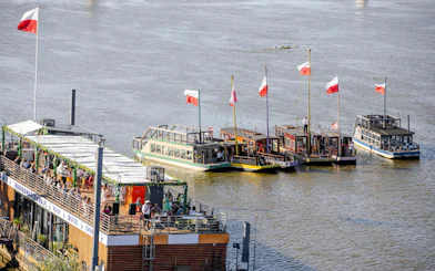 Traditional Galar boats docked on Vistula River in Warsaw, Poland, with Polish flags.