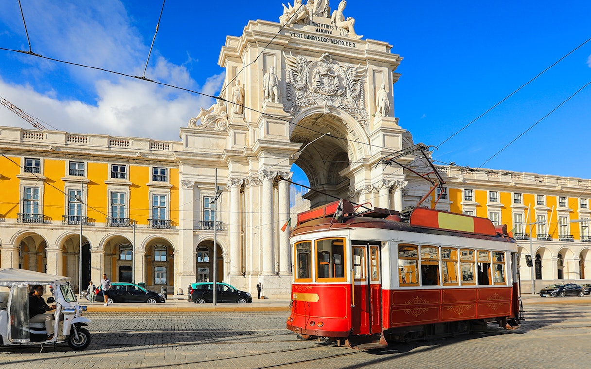 Lisbon tram passing by the Arco da Rua Augusta in a sunny city square.