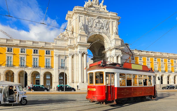 Lisbon tram passing by the Arco da Rua Augusta in a sunny city square.
