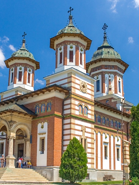 Peles Castle with visitors in front, surrounded by trees, under a clear blue sky.