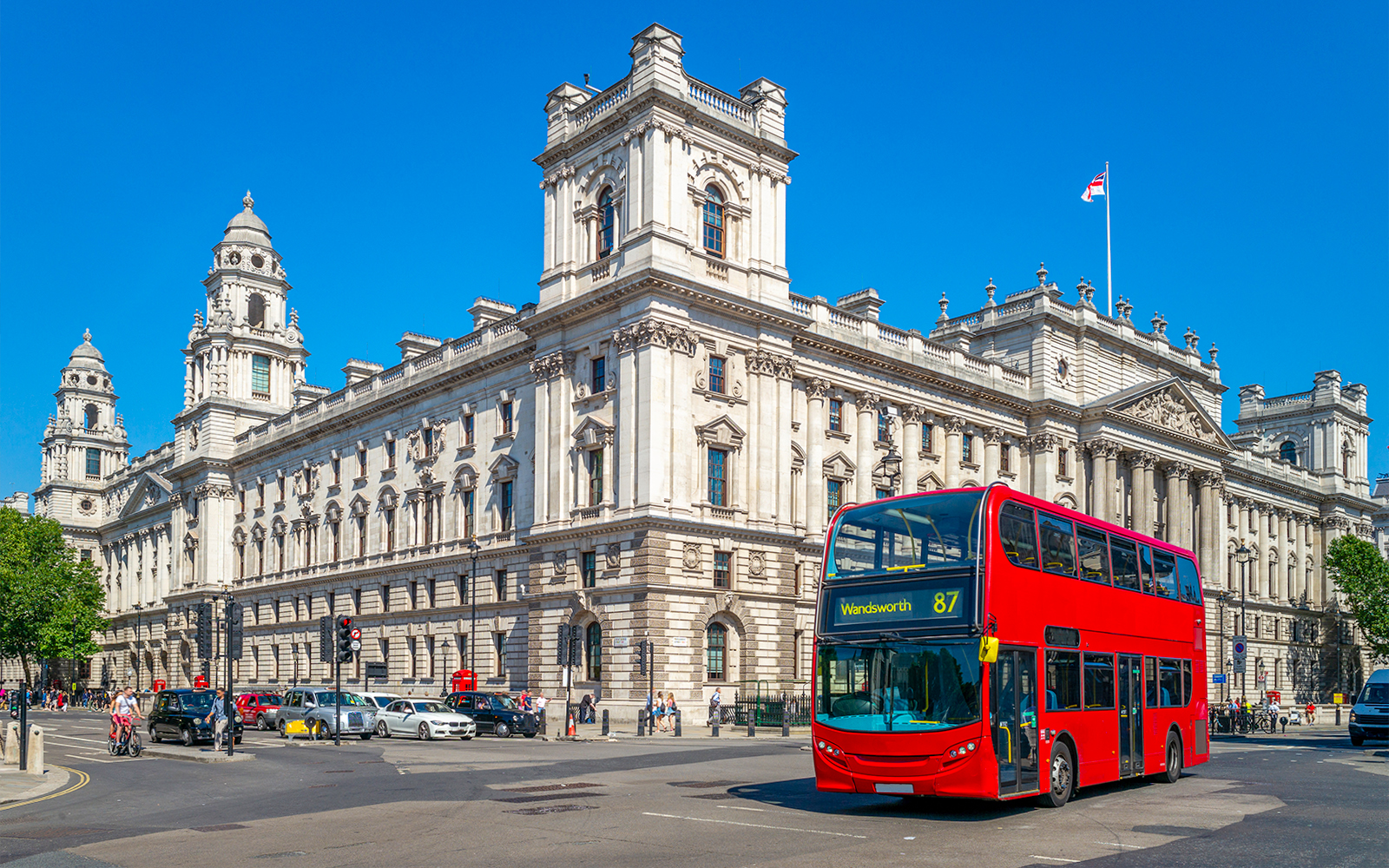Red double-decker bus on London street near historic building.