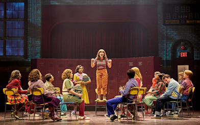 Group of students in a school setting, one standing on a chair, from Stranger Things: The First Shadow.