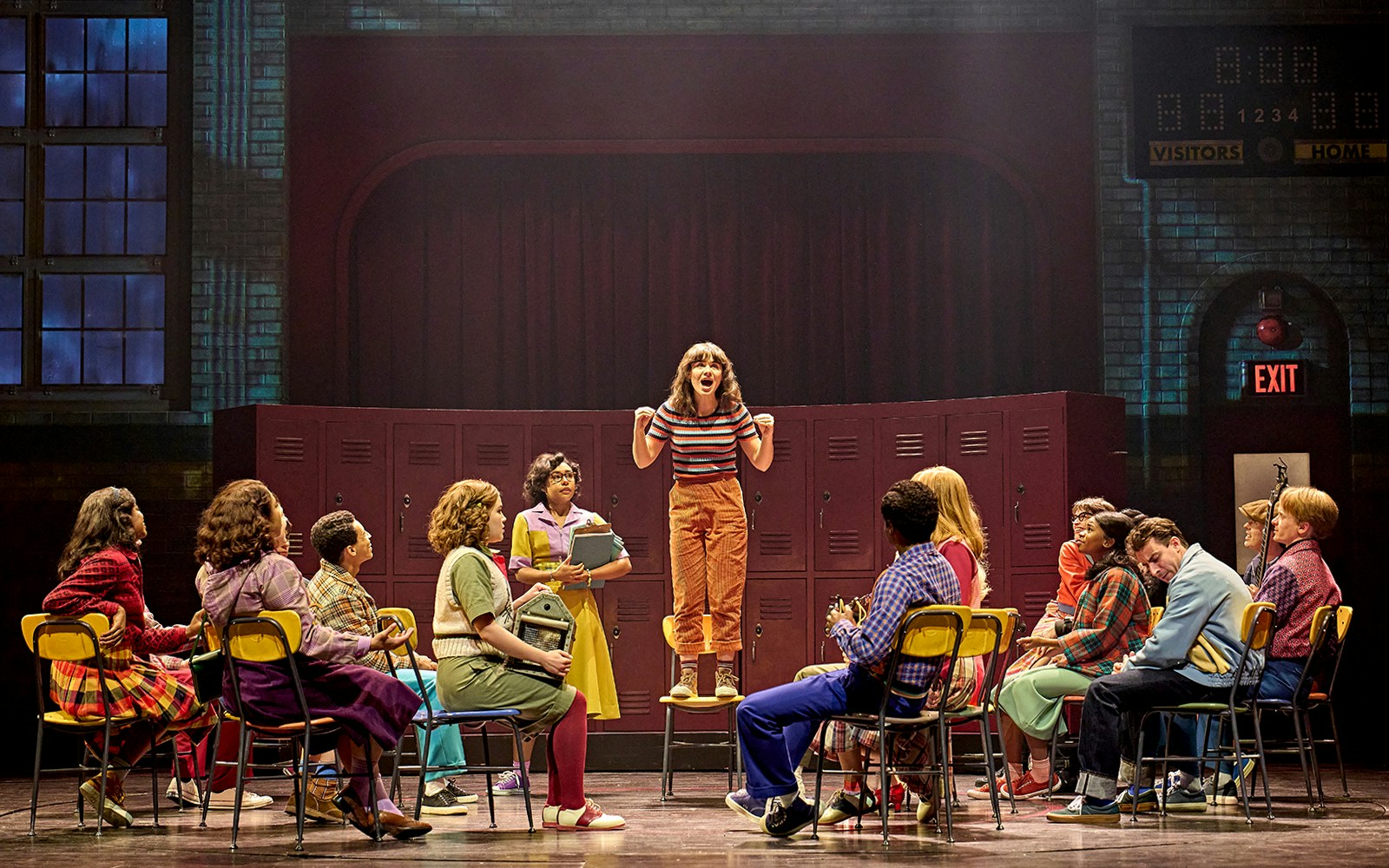 Group of students in a school setting, one standing on a chair, from Stranger Things: The First Shadow.