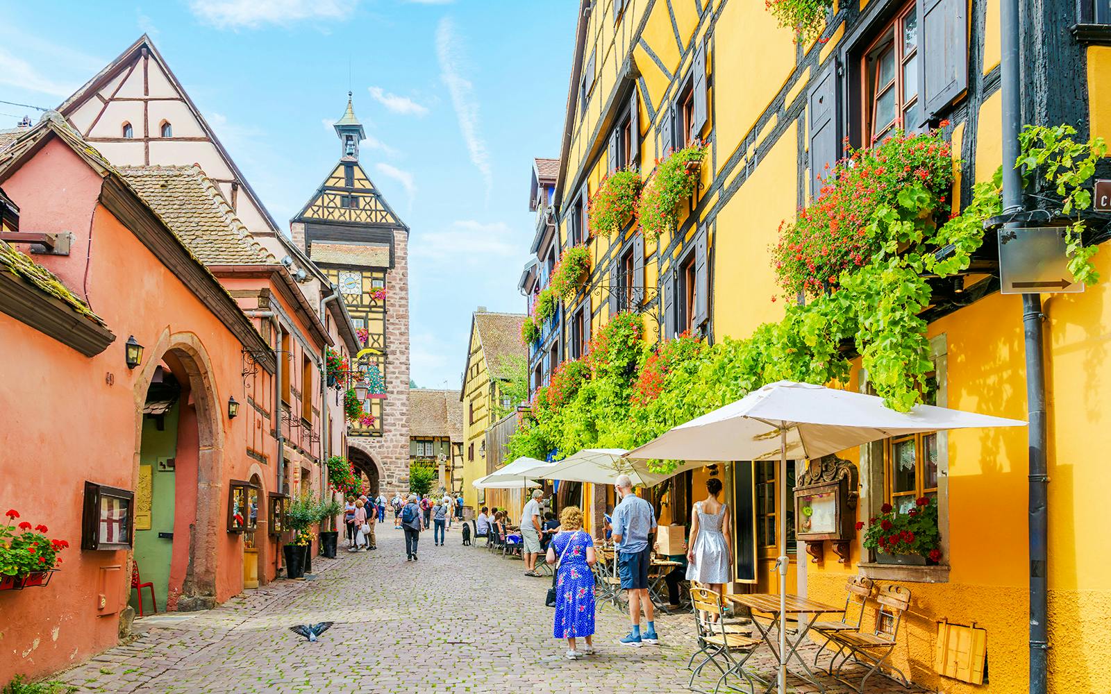 Dolder Belfry Clock Tower in Riquewihr, France, with colorful half-timbered buildings and cobblestone street.